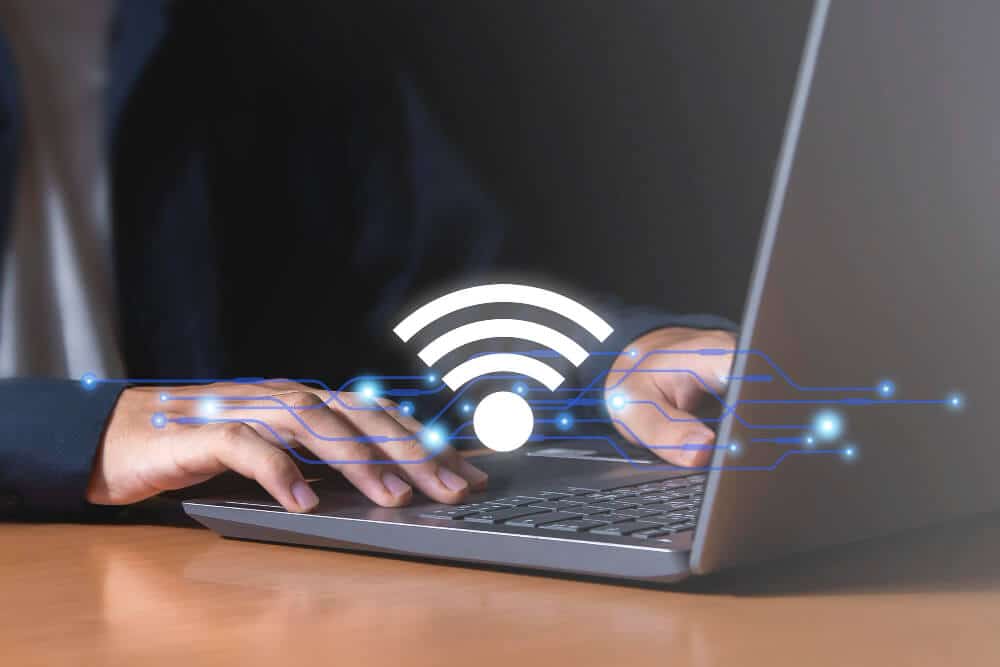 homem mexendo no notebook, com sinalização de wifi, se conectando na internet da empresa