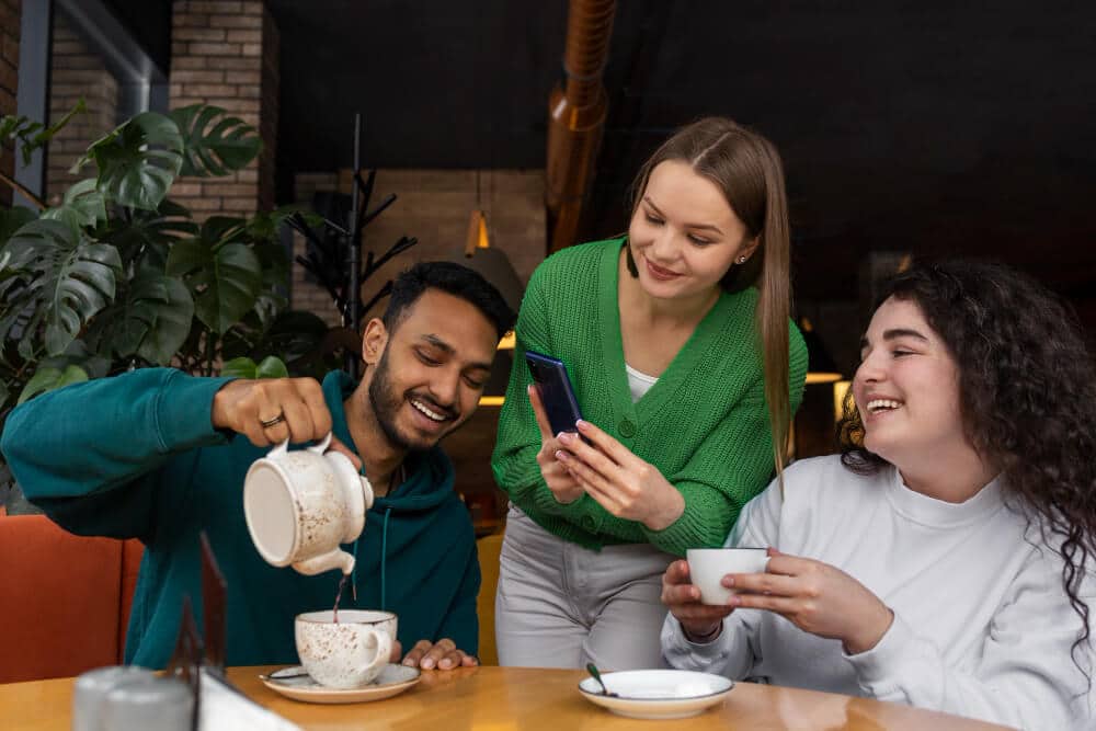 amigos em uma cafeteria colocando café e a amiga tirando foto com um celular, simboliza como a cafeteria consegue atrair leads mais qualificados transformando esses visitantes em oportunidades reais