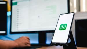 pessoa mexendo no no computador com a tela aberta no WhatsApp e o celular com a logo do WhatsApp, simbolizando qual o melhor whatsapp para empresa