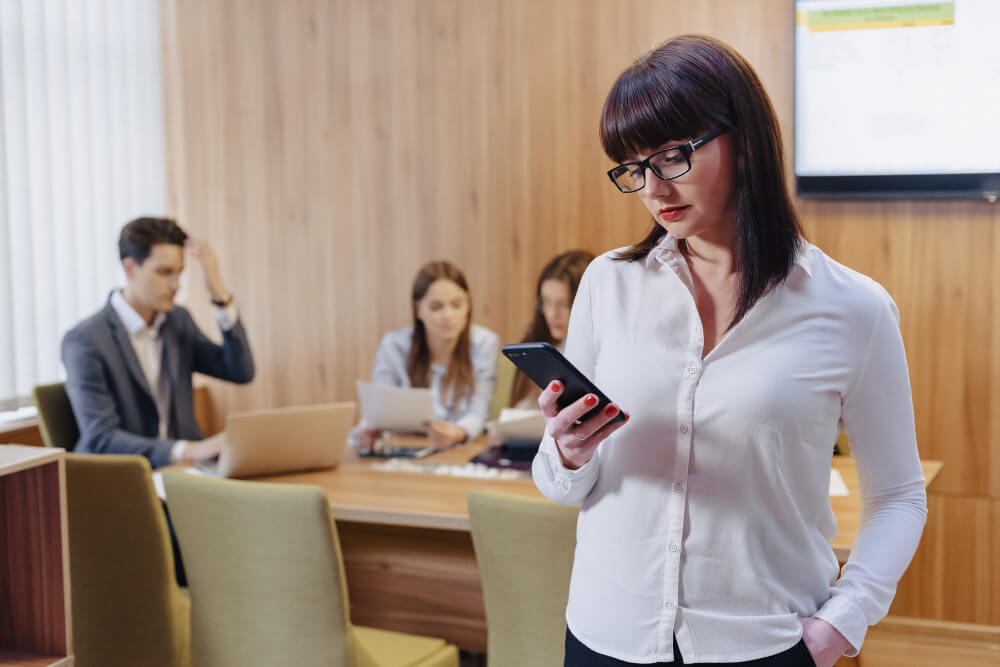 Pessoas trabalhando em um escritório e uma mulher em destaque porém preocupado mexendo no celular simbolizando Como usar o WhatsApp Business com múltiplos usuários sem virar bagunça no atendimento